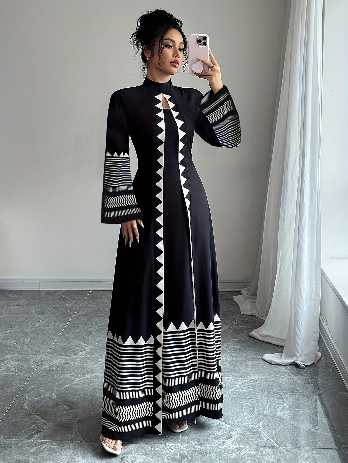 Woman taking a mirror selfie wearing a black and white patterned dress.