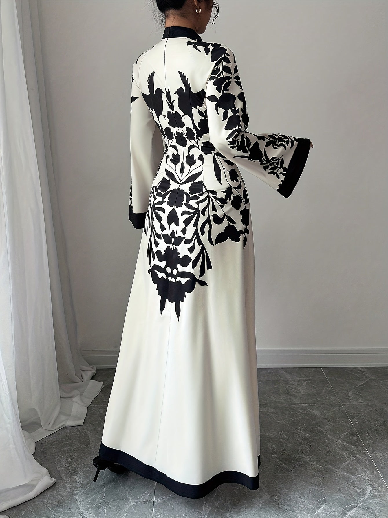 White dress with black floral pattern worn by a person, standing against a neutral background.