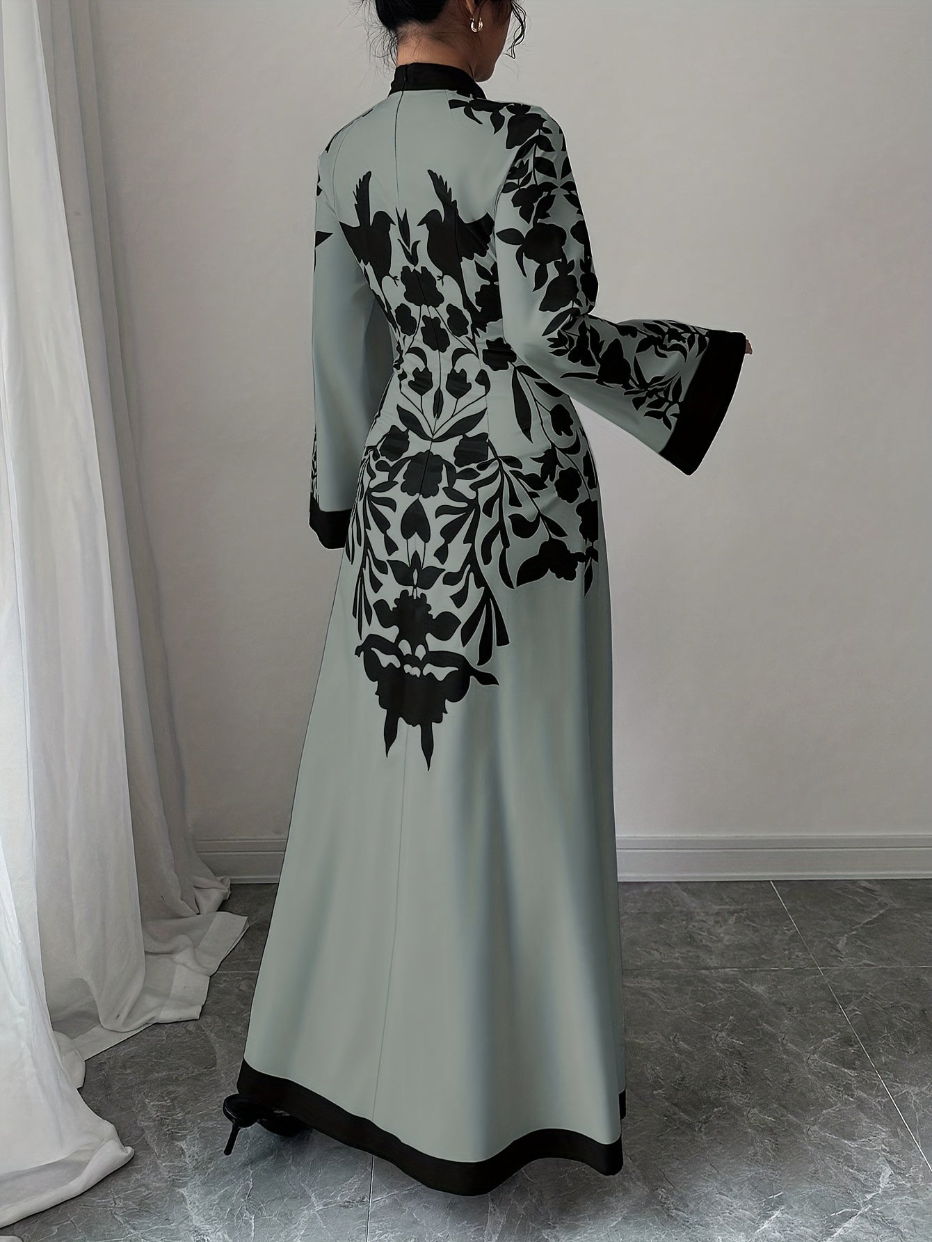 Long light green dress with black floral patterns worn by a person, standing against a neutral background.