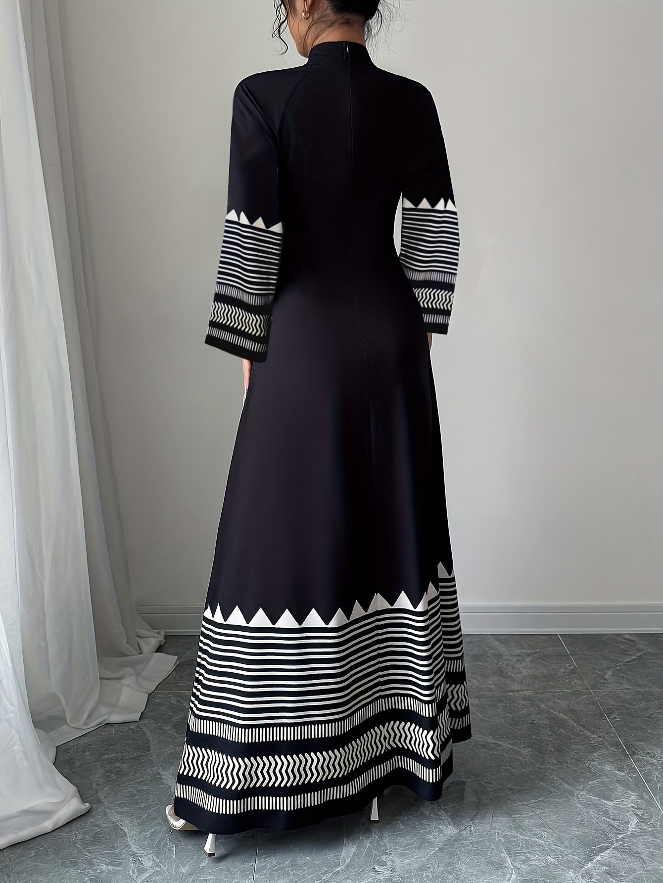 Person wearing a black dress with white geometric patterns in a minimal indoor setting.