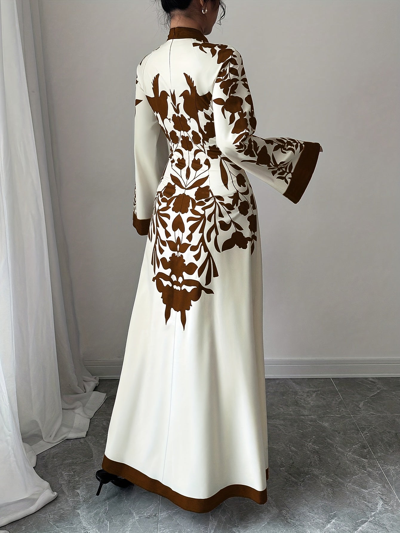 Long white dress with brown floral patterns worn by a person in a minimal indoor setting.