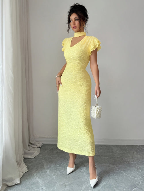 A woman models a pale yellow textured midi dress with a high mock neck, ruffled cap sleeves, and a keyhole cutout at the collar. She is wearing white pointed-toe heels and holding a small white beaded handbag, standing in a room with a gray floor and light gray wall.