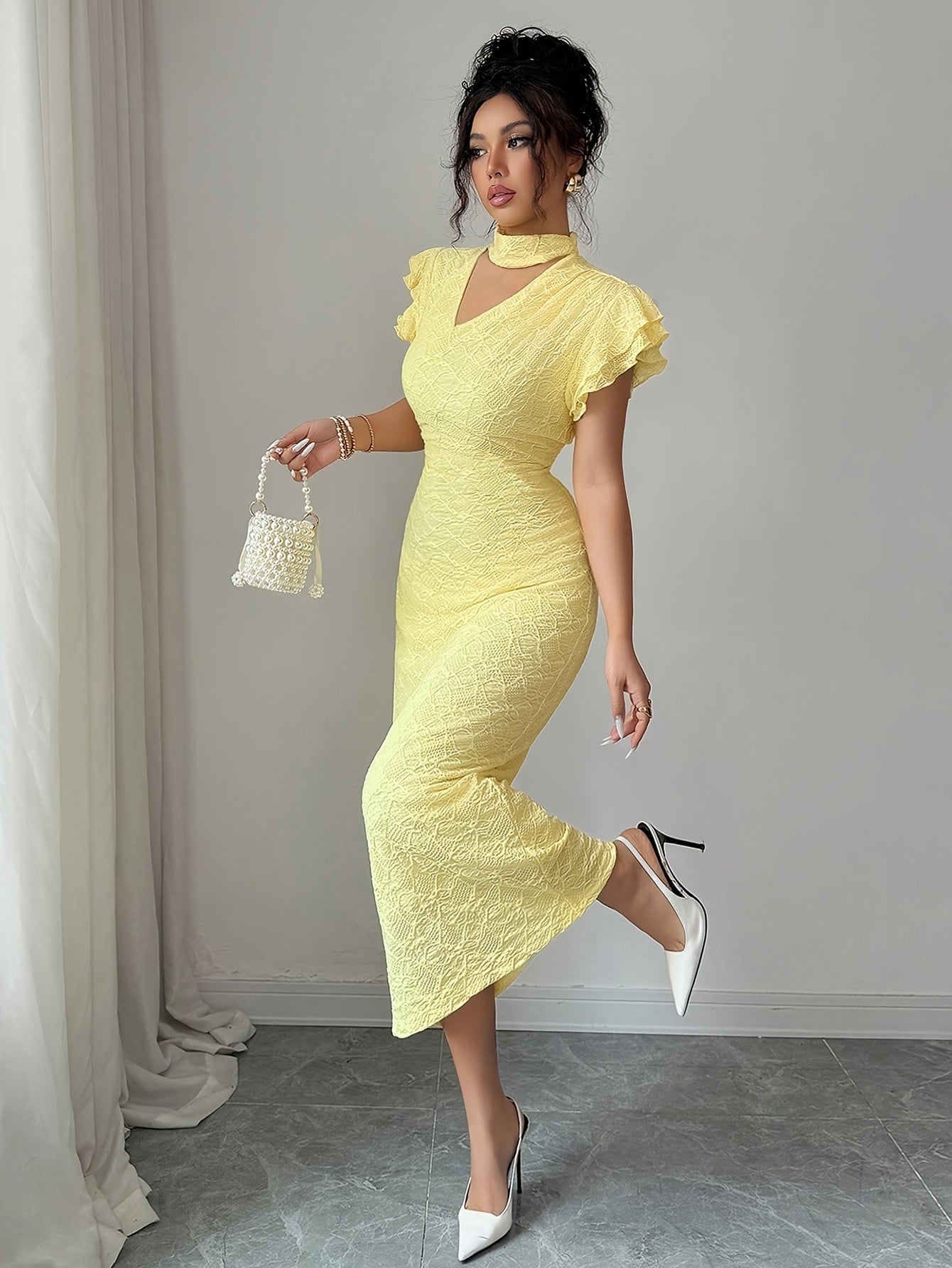 A woman models a pale yellow textured midi dress with ruffled short sleeves, a high keyhole neckline, and a fitted silhouette. She is holding a small white woven handbag and wearing white pointed-toe heels, standing in a room with a gray floor and light gray wall.