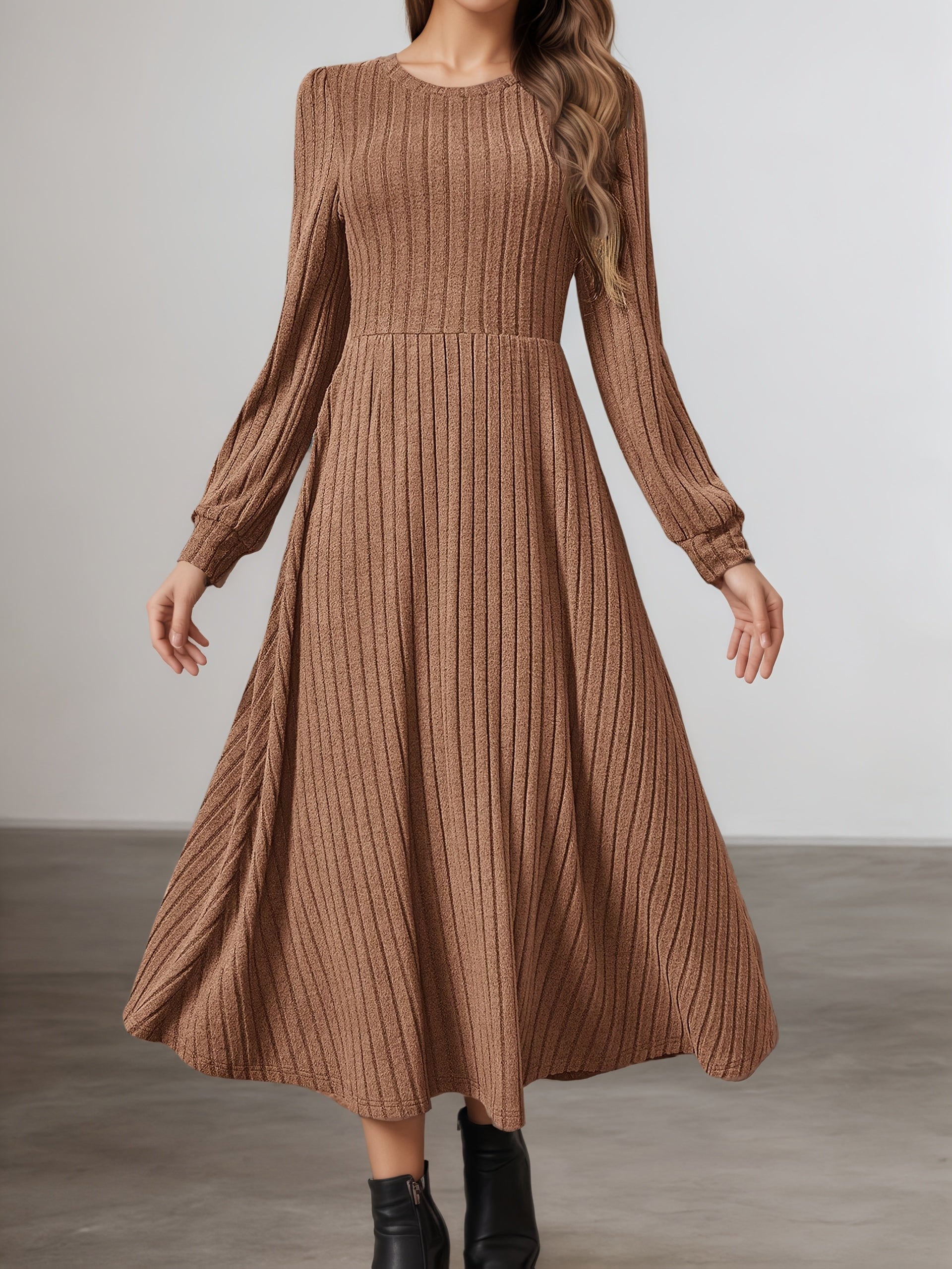 A woman wearing a brown ribbed knit long-sleeve midi dress with a flared skirt, paired with black ankle boots, standing against a neutral studio background.