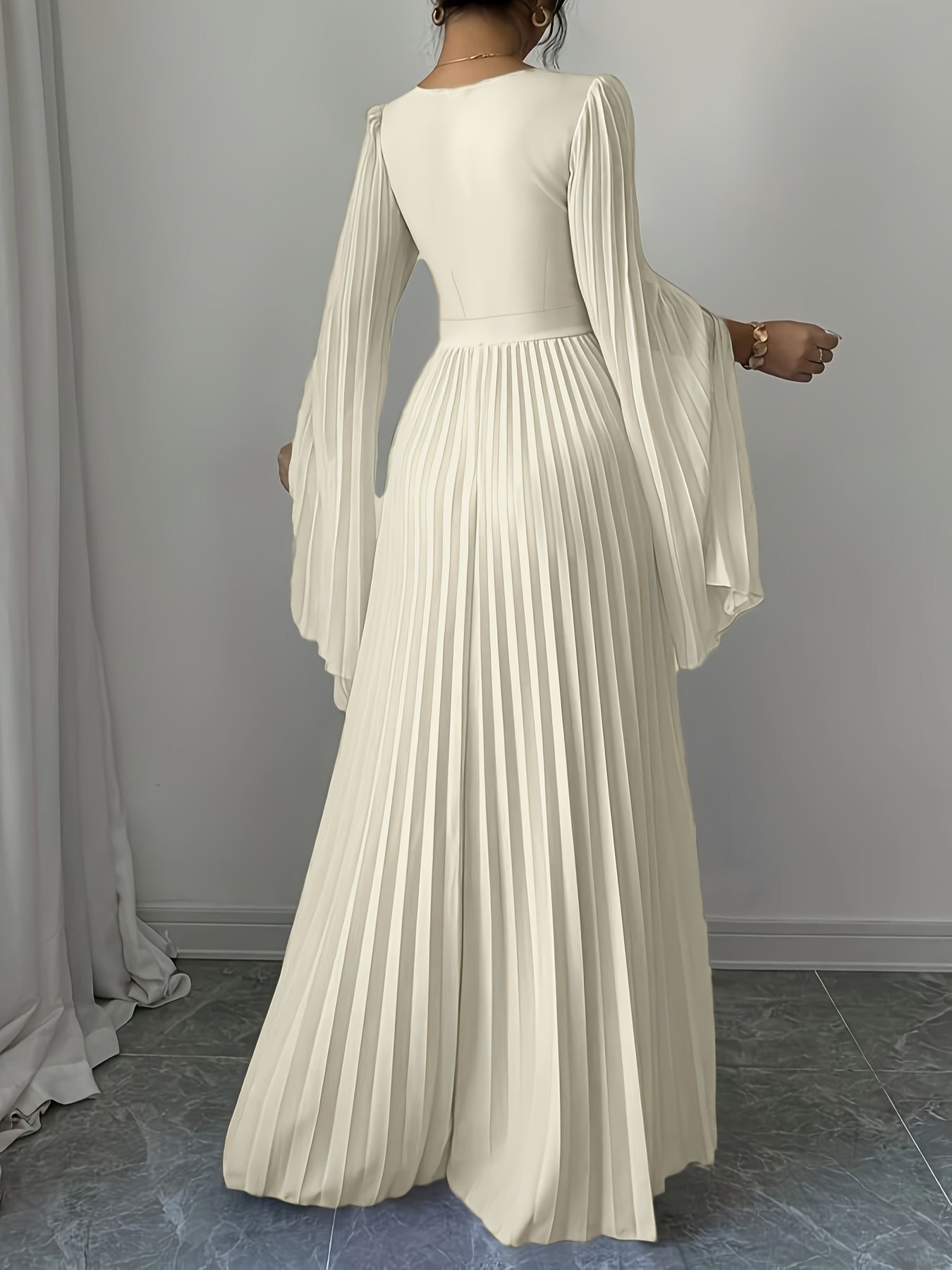 An off-white/cream maxi dress with long bell sleeves and a pleated skirt, shown from the back on a model in an indoor setting.