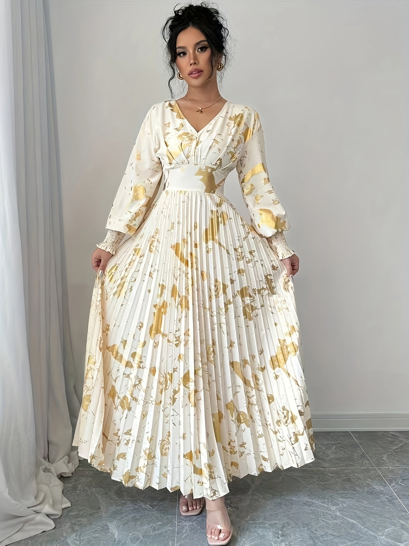 Woman wearing a long, floral-patterned dress with pleated skirt against a neutral background