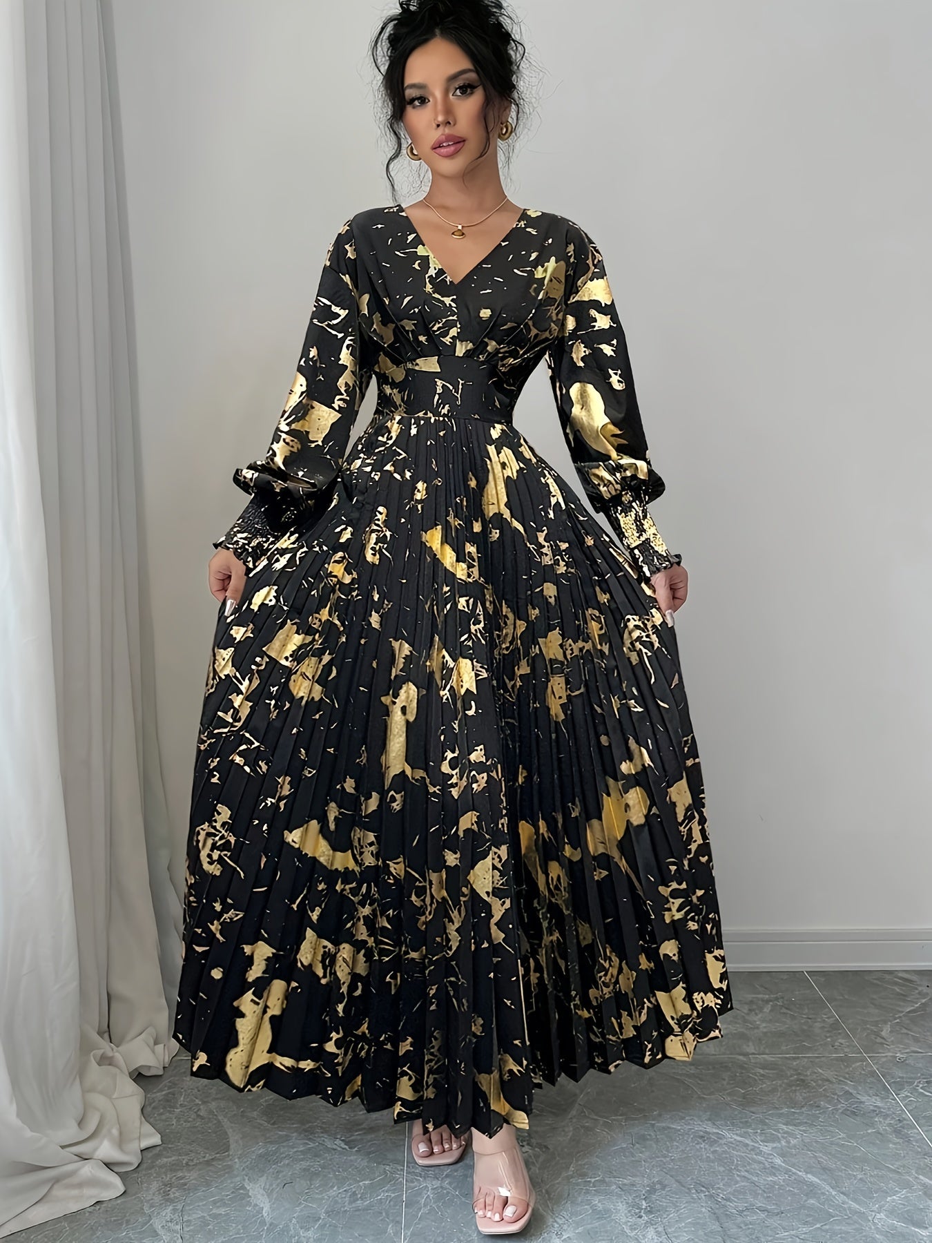 A woman modeling a long-sleeved black maxi dress with a gold abstract marble pattern, standing in a room with gray tiled floors and a light gray wall.