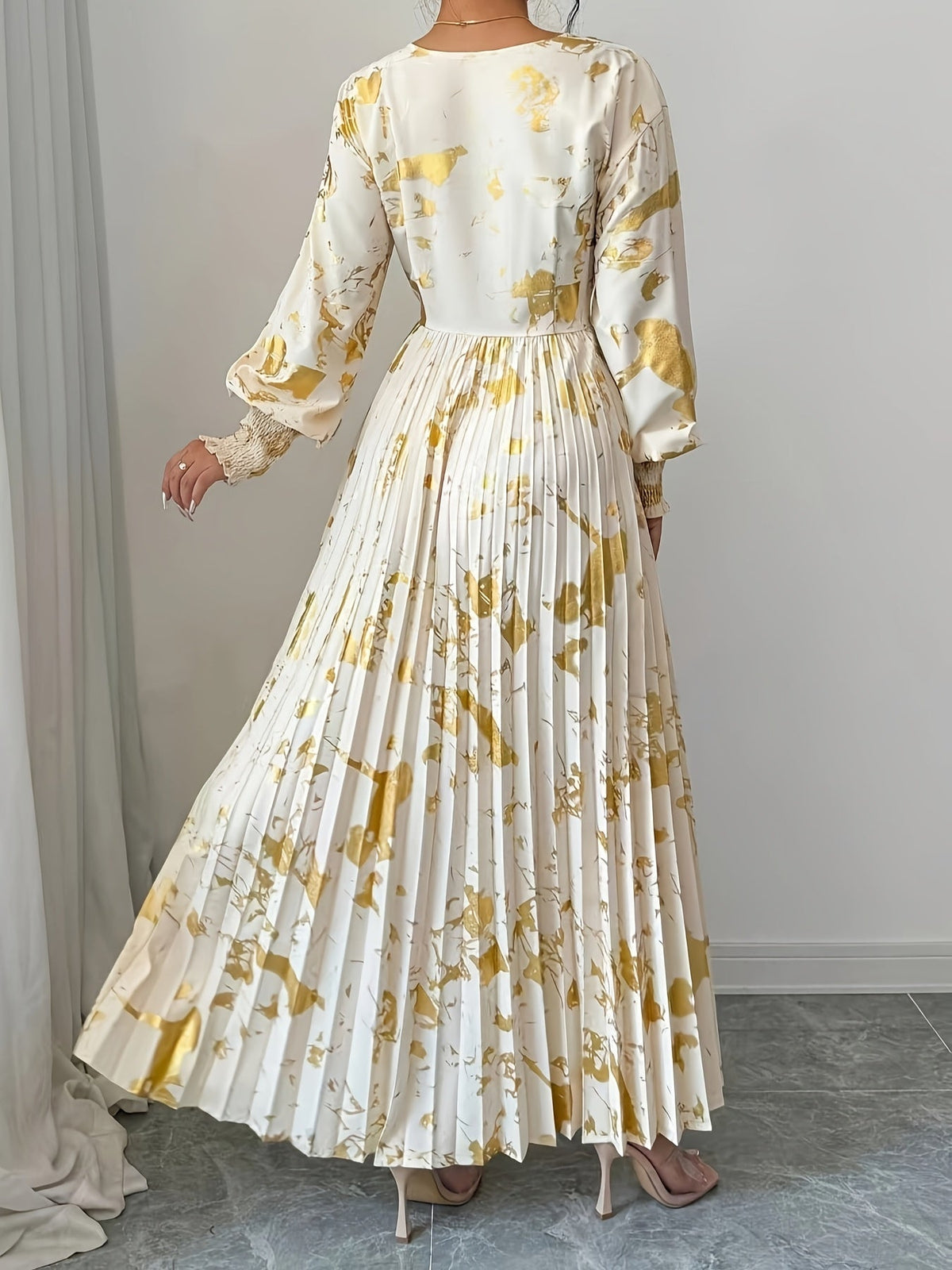 White dress with gold floral pattern worn by a person against a plain background