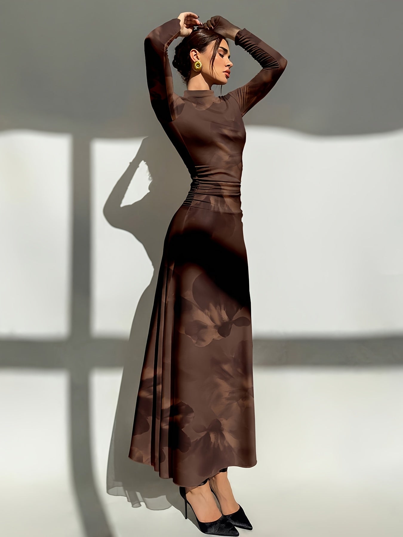 Woman wearing a brown dress with a high collar and long sleeves against a white wall.