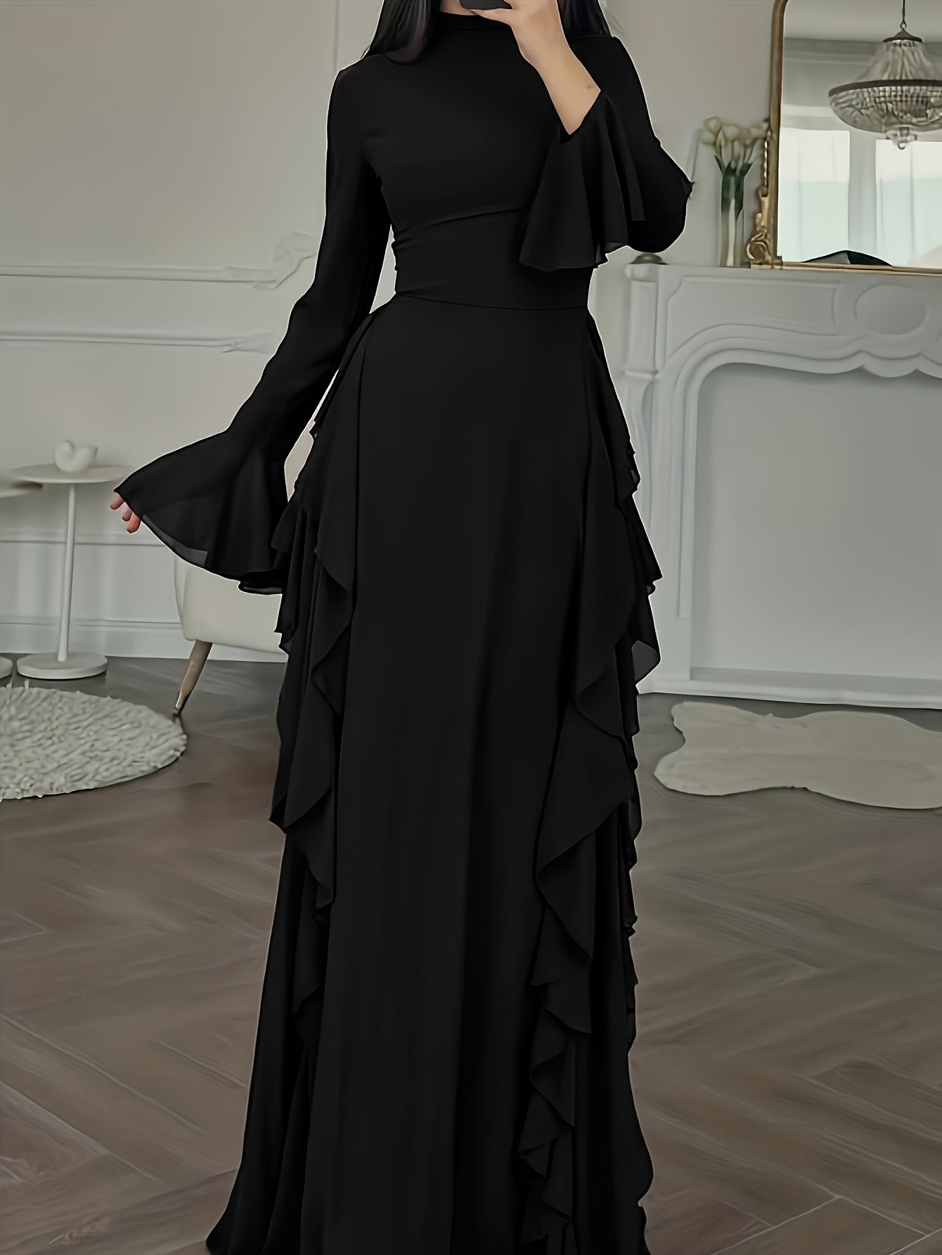 Black ruffled dress worn by a person in a room with white walls and a fireplace.