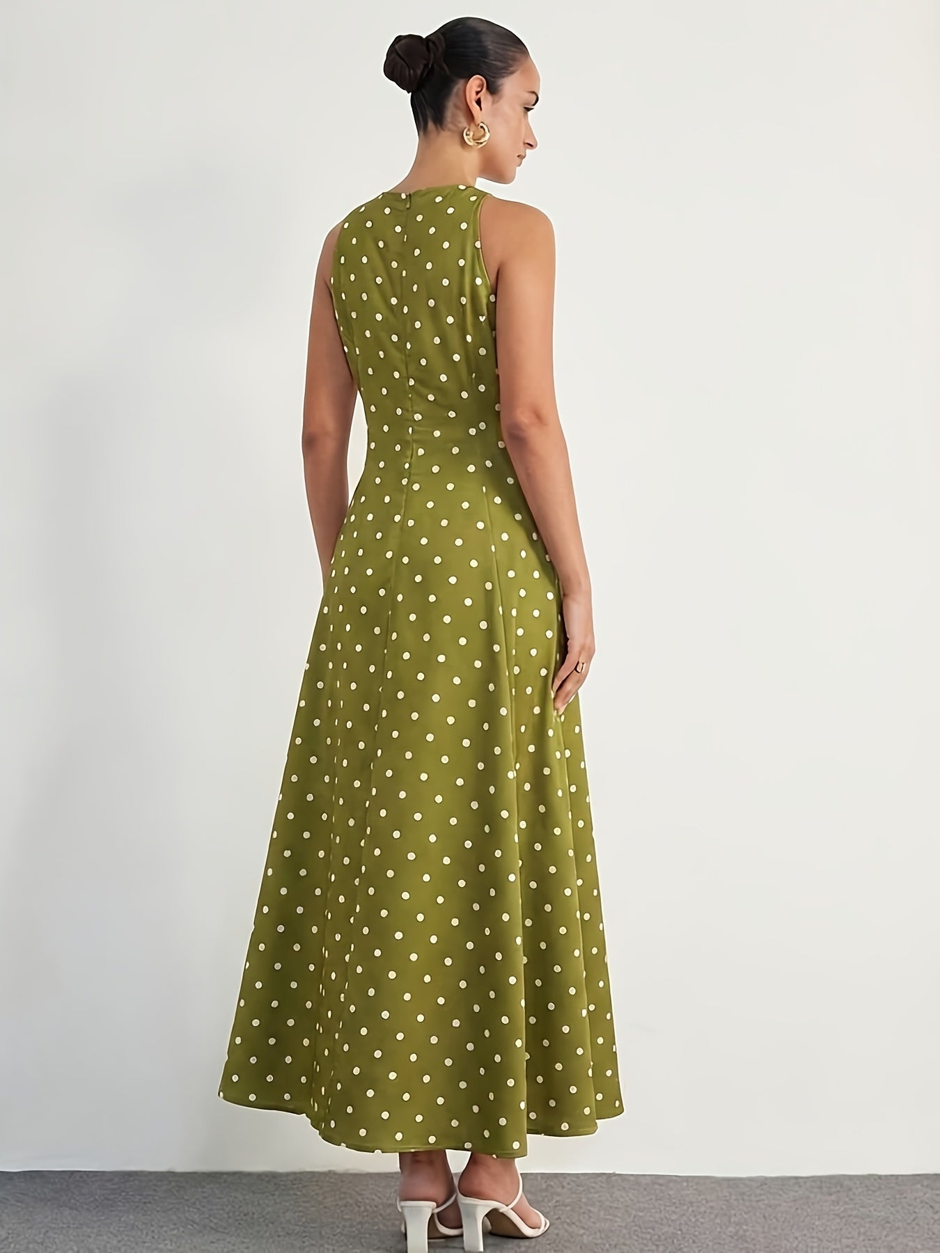 A woman wearing a sleeveless olive green maxi dress with a white polka dot pattern, shown from the back against a plain white studio background.