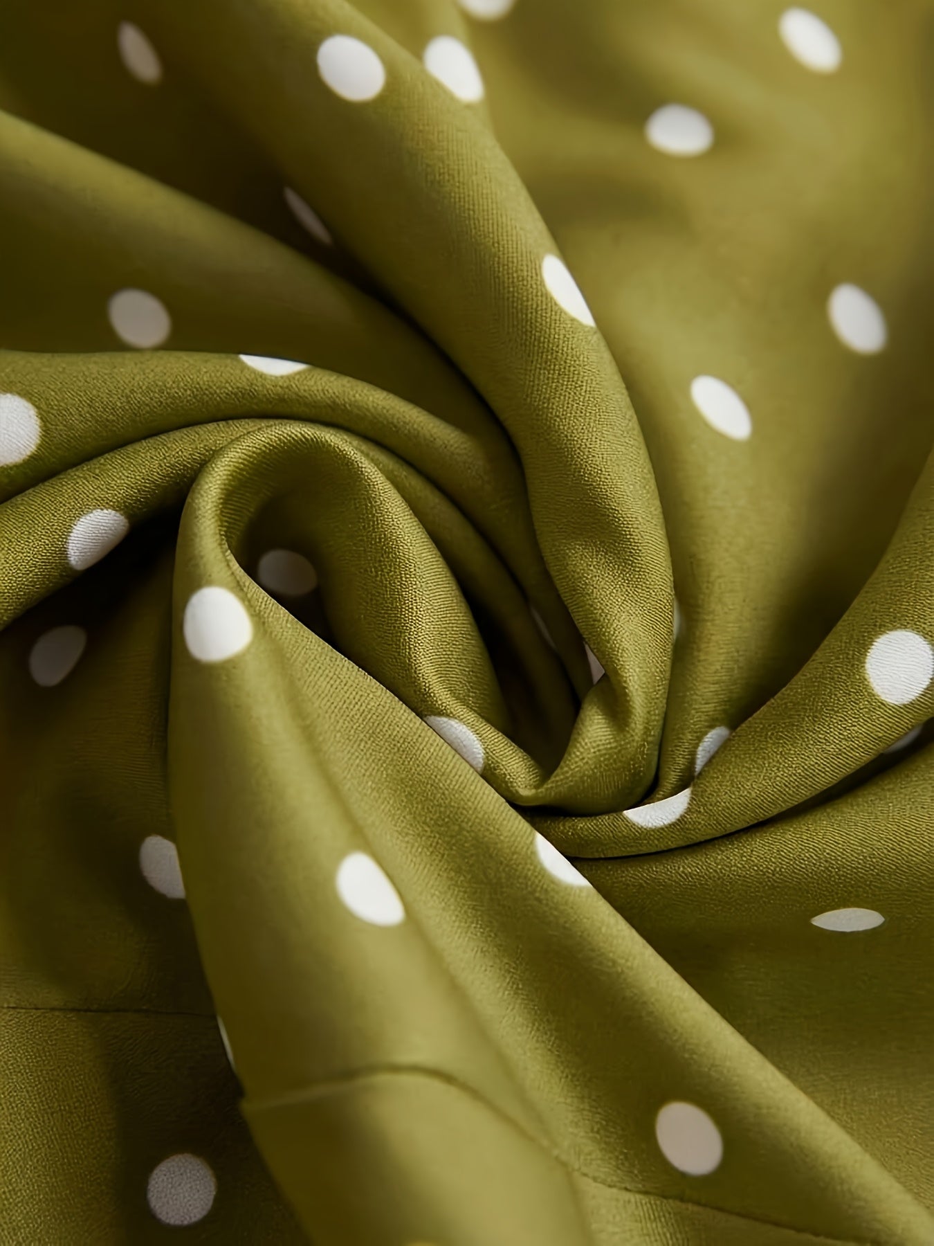 Olive green fabric with a white polka dot pattern, styled in a swirl to show its texture and drape.
