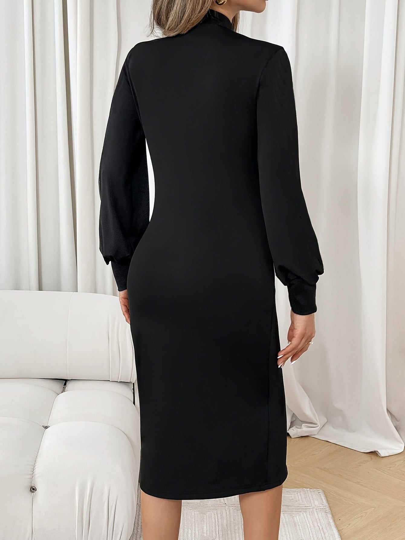 Black dress with sheer sleeves worn by a person, standing against a white curtain background.