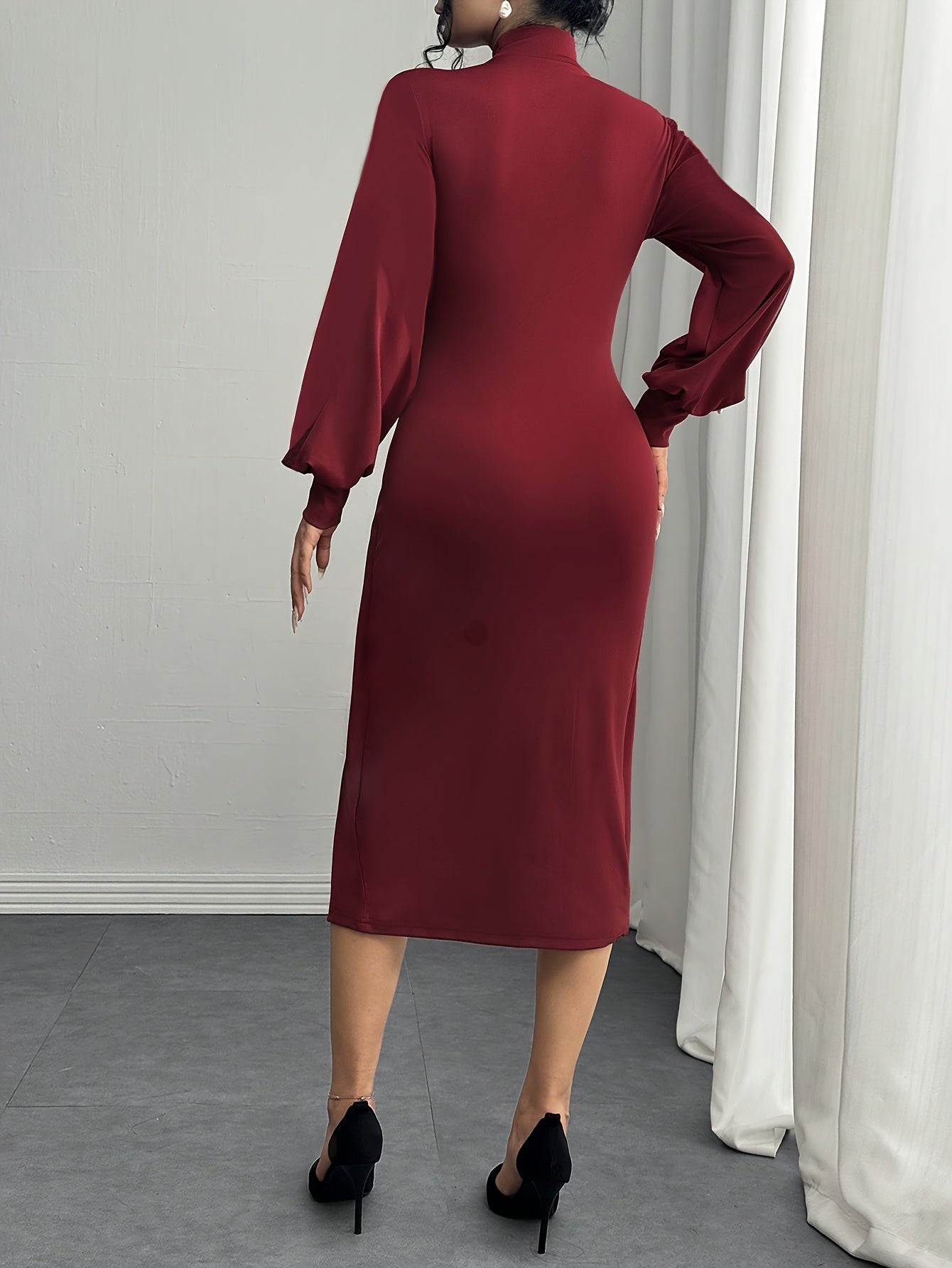 A woman wearing a long-sleeved, high-neck midi dress in deep burgundy, shown from the back. She is wearing black high heels and standing in a room with a gray floor, a light gray wall, and white curtains.