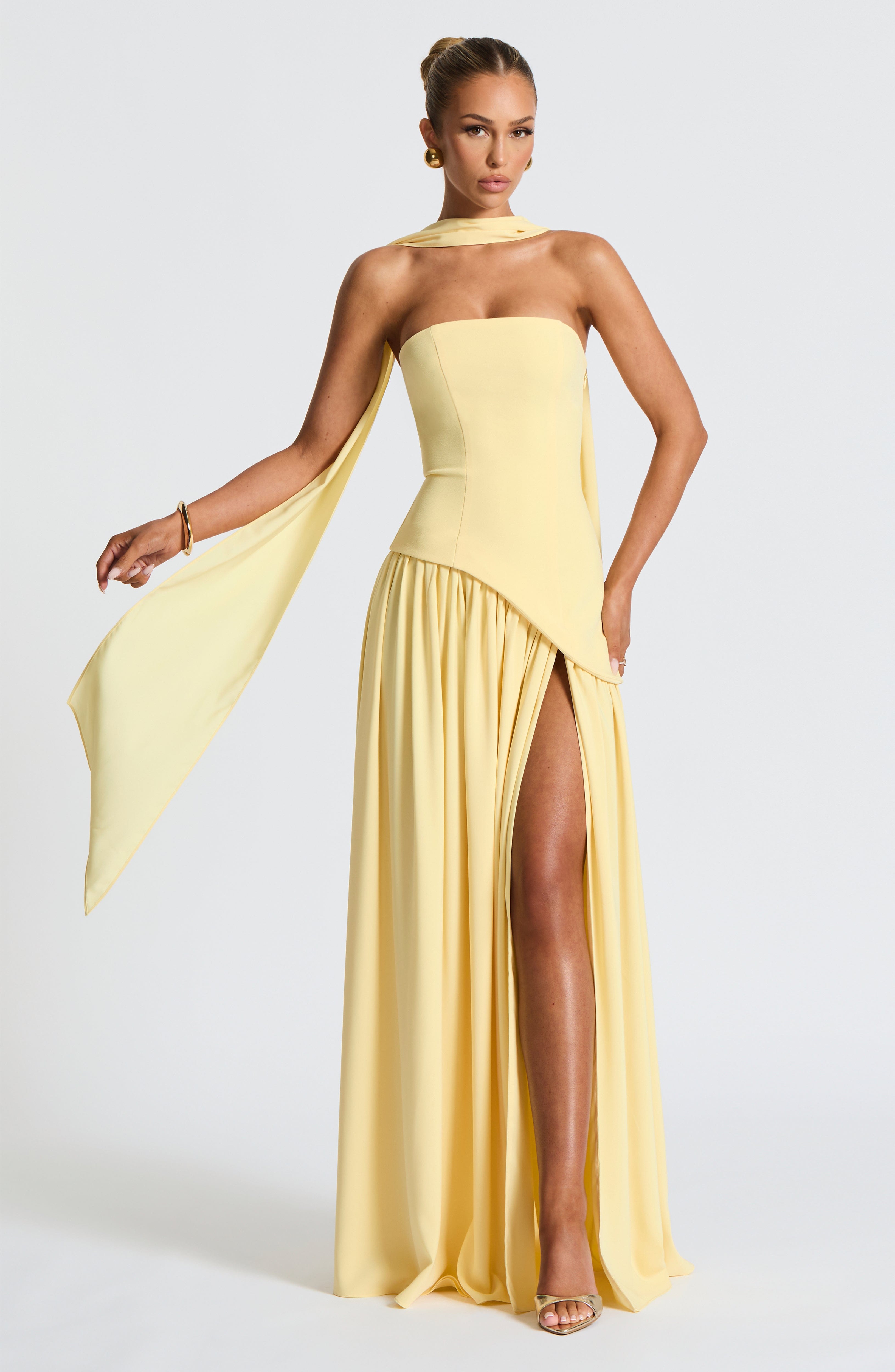 Woman wearing a yellow strapless gown with a slit on a white background