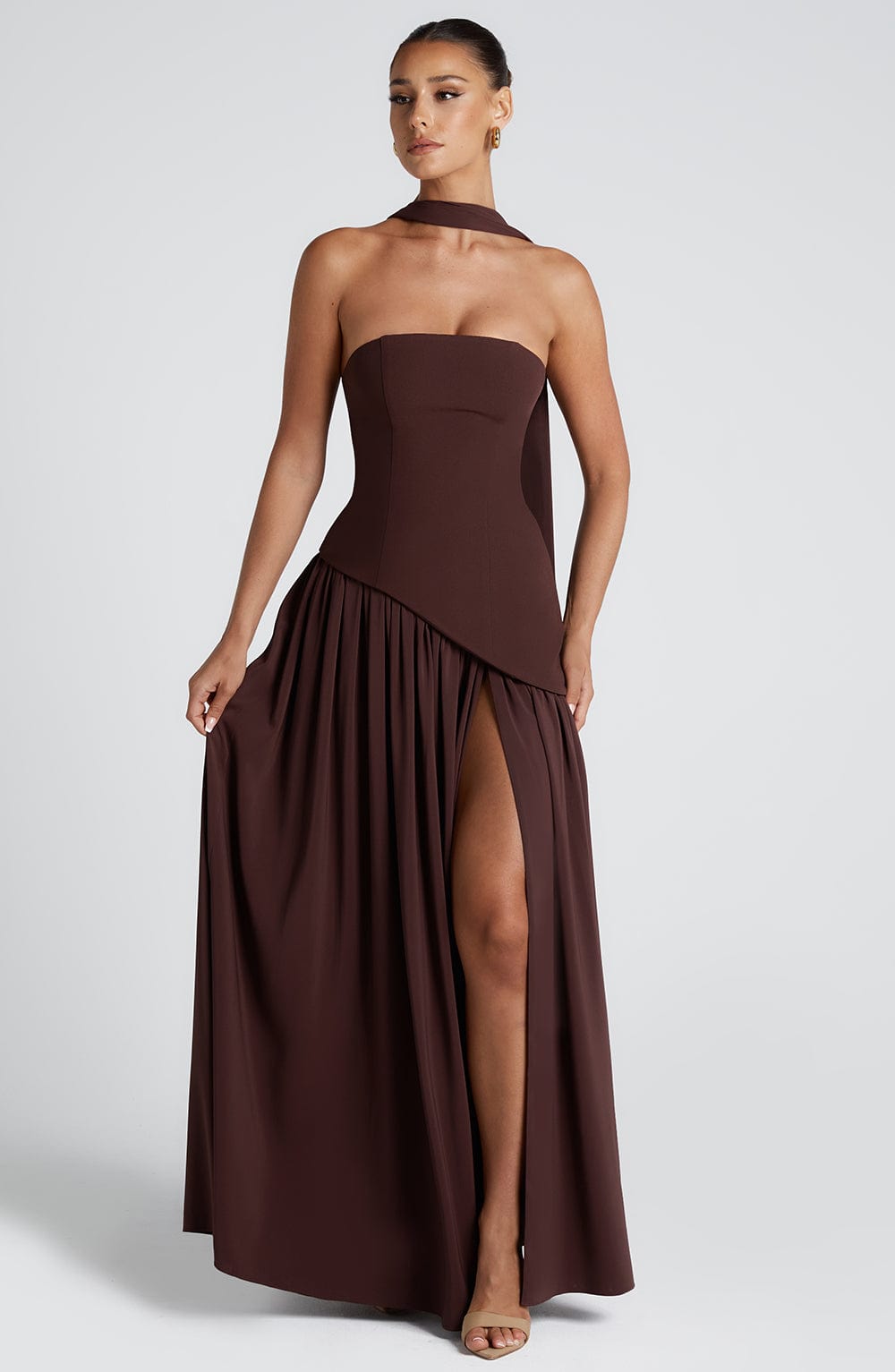 Woman wearing a brown strapless gown with a slit on a white background