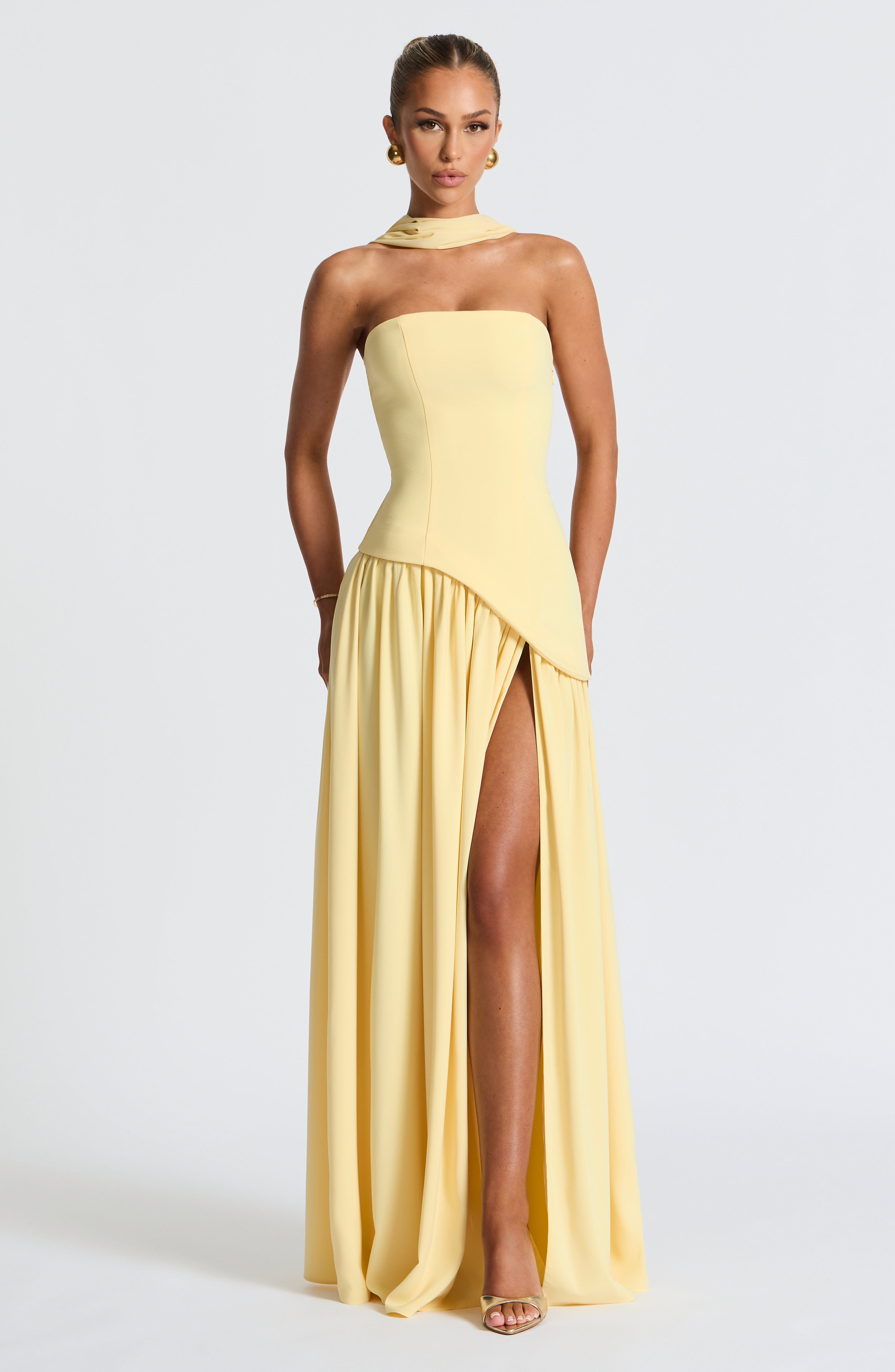 Woman wearing a yellow strapless gown with a slit on a white background