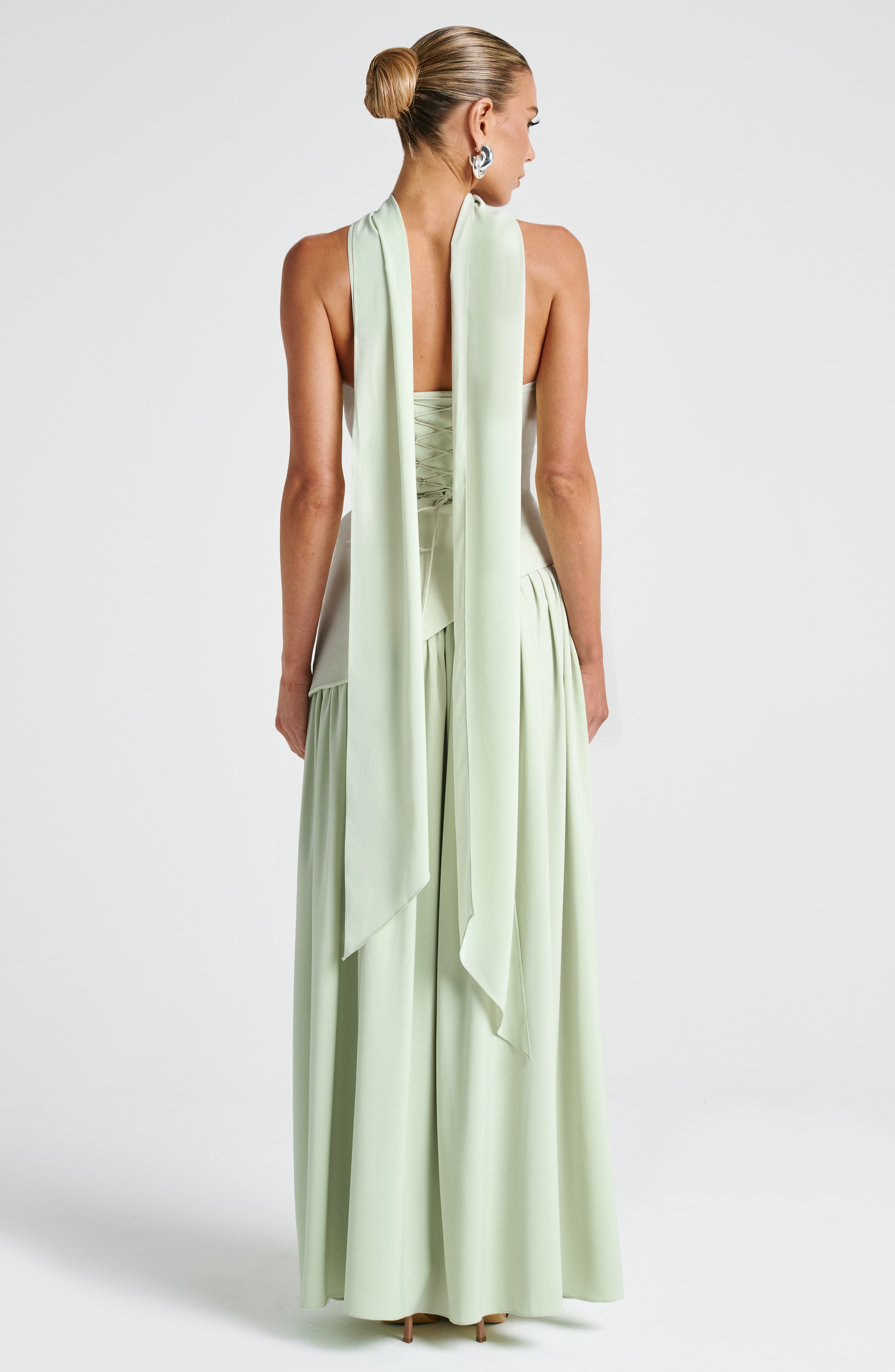 Woman wearing a light green dress with a flowing scarf on a white background