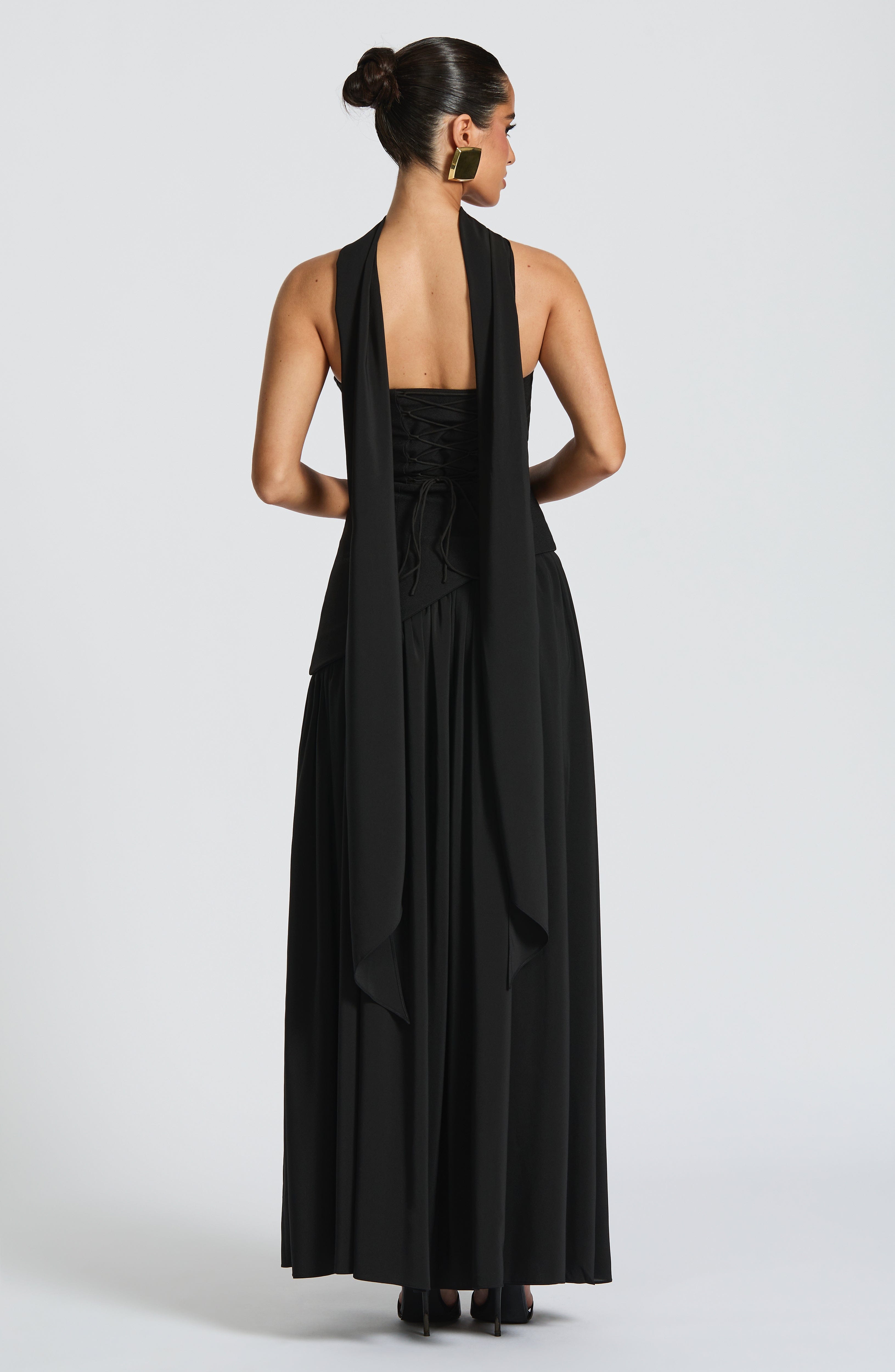 Woman wearing a black halter neck dress with a draped design on a white background