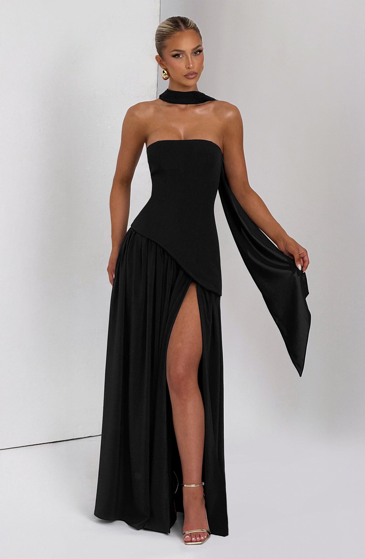 Woman wearing a black strapless gown with a slit on a white background