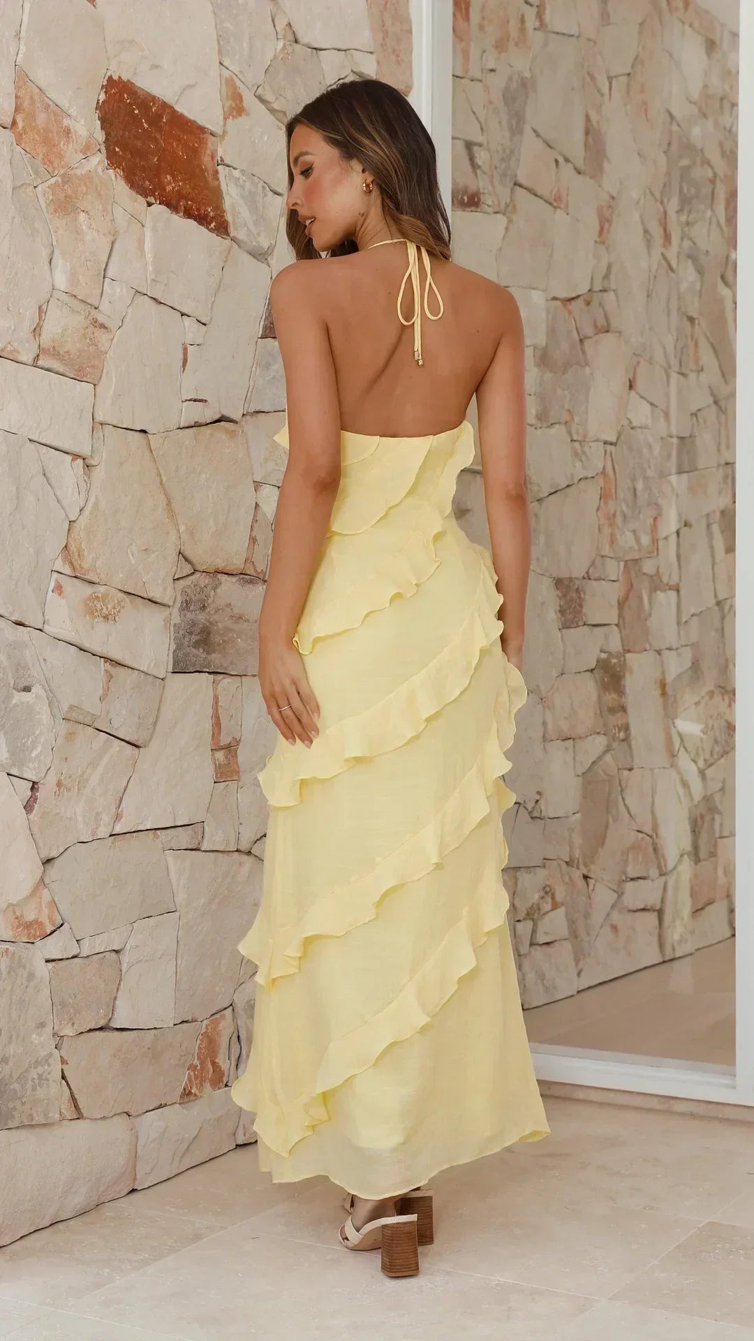 Woman wearing a yellow ruffled dress against a stone wall.