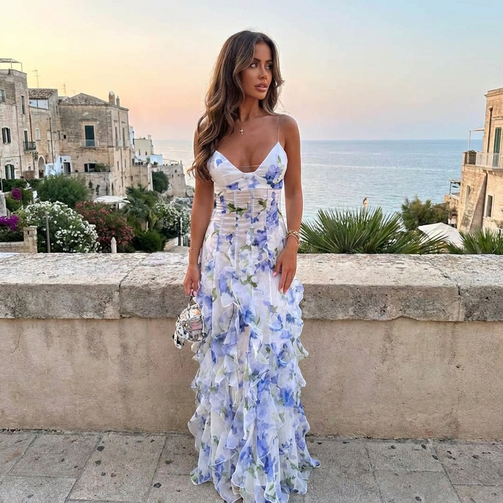 Woman in a floral dress standing by a scenic coastal town.