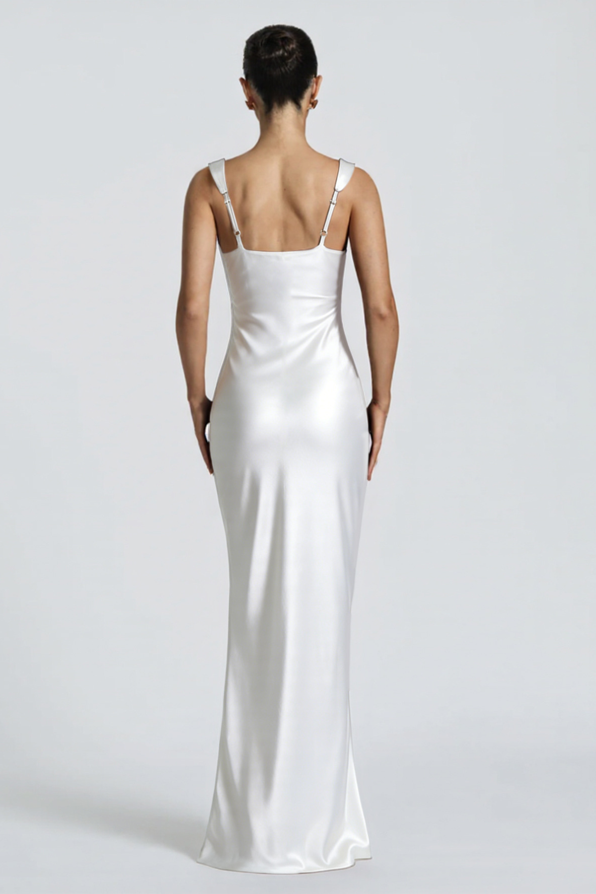 Woman wearing a white satin gown with thin straps on a plain background