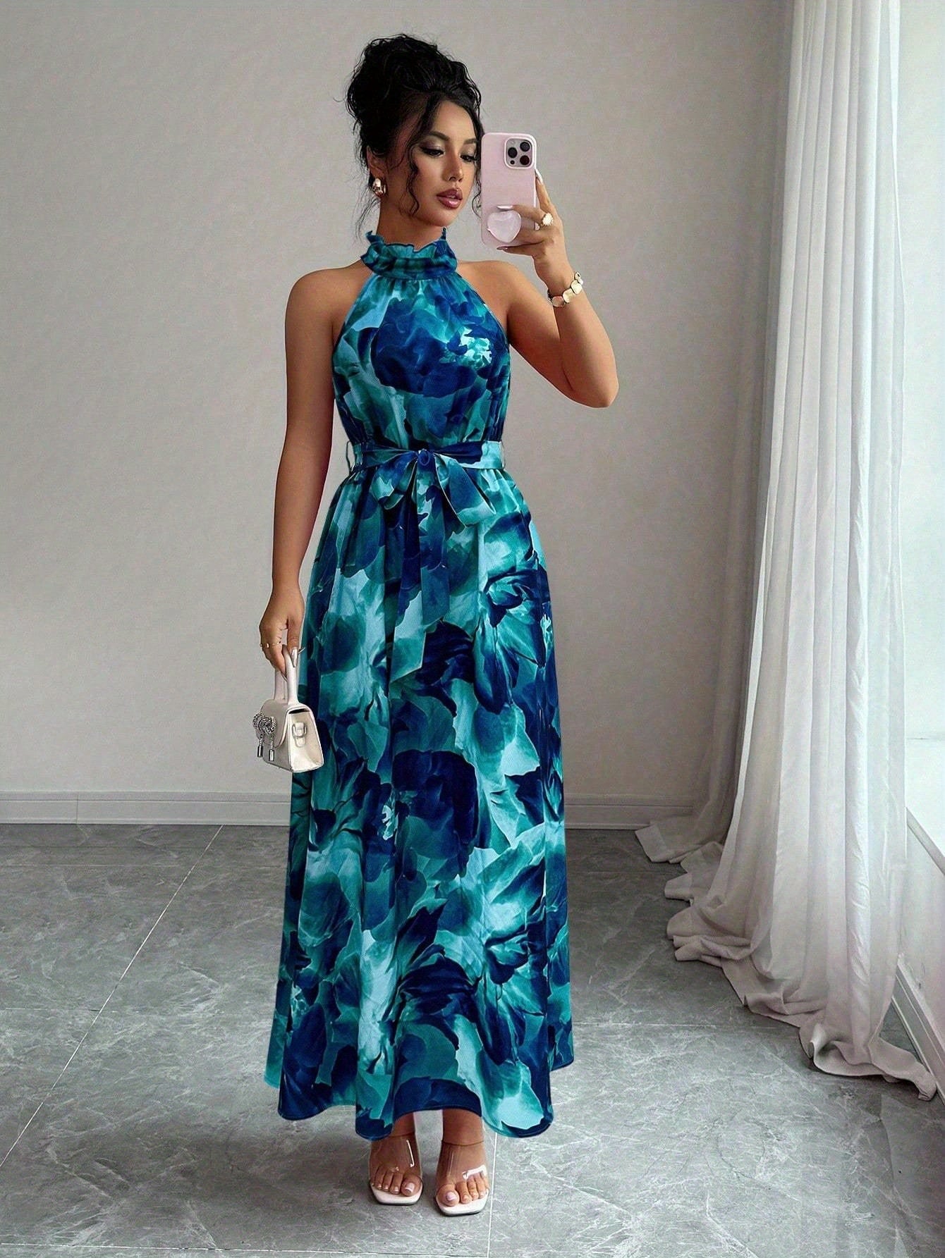 Woman taking a mirror selfie wearing a blue floral dress in a room with white curtains.